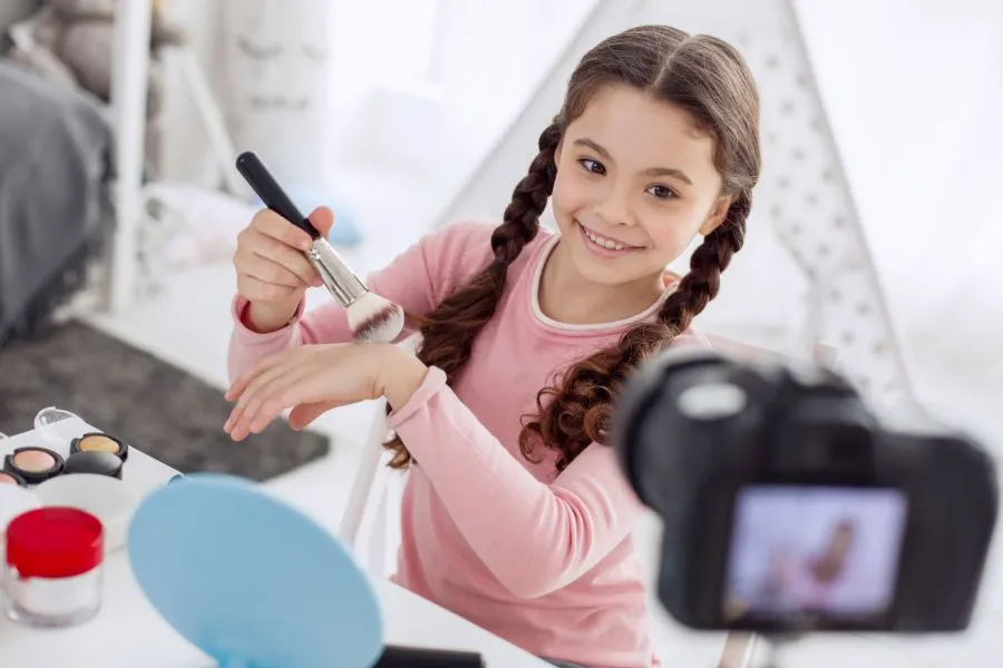 A kid in front of a camera doing her makeup.